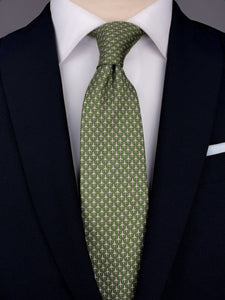 Olive green mulberry silk twill tie with a microprint of airplanes in a shade of grey. The tie is worn with a white shirt and a navy blue suit. 