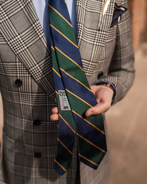 Man wearing a grey prince of Wales check suit with a green and navy blue striped regimental necktie