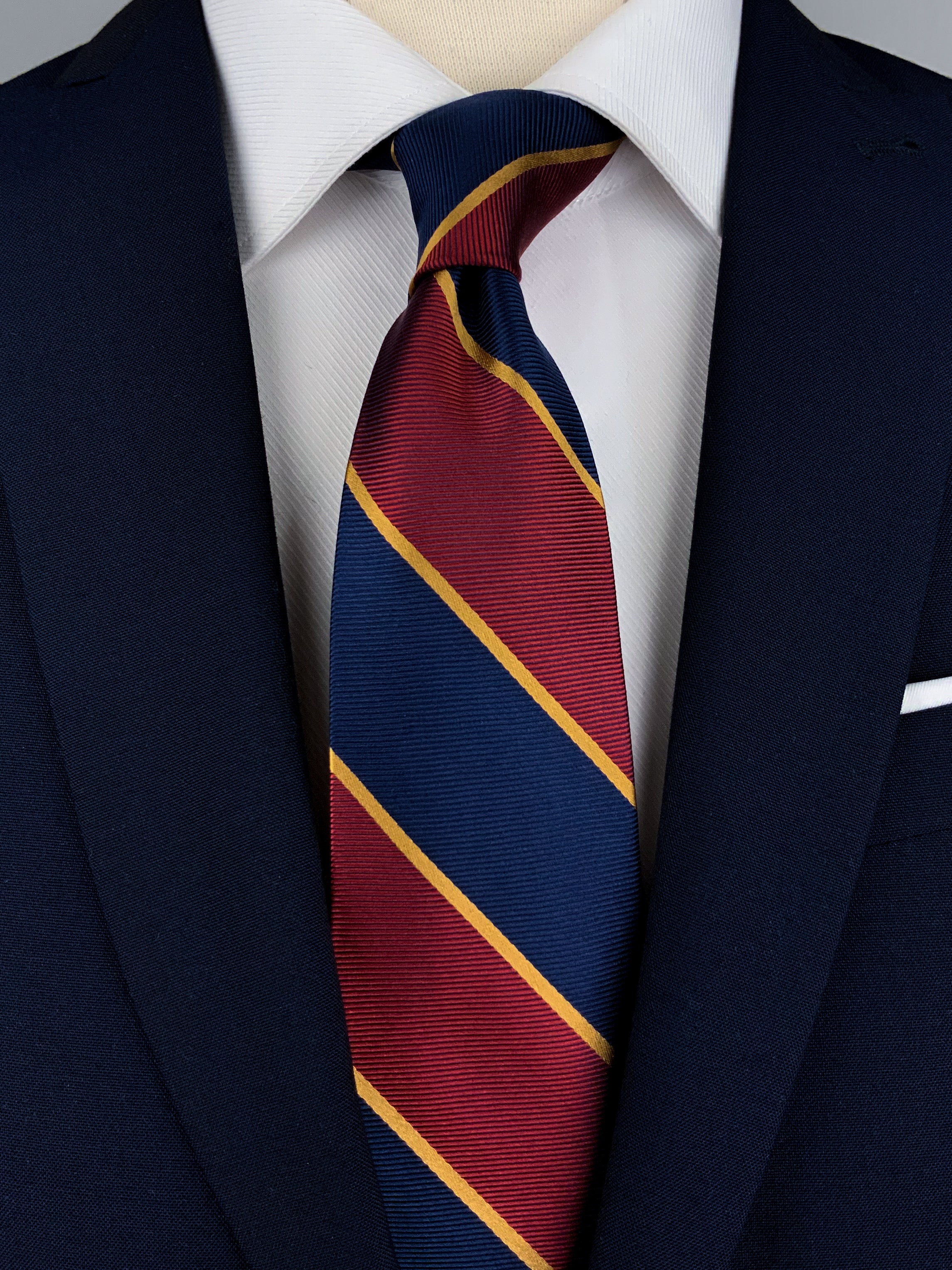 Mulberry silk twill regimental tie with navy blue and red diagonal stripes with woven gold detailing worn with a white shirt and a navy blue suit