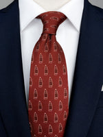 A burgundy red tie with a pattern of ships printed on top worn with a white shirt and a navy blue suit.