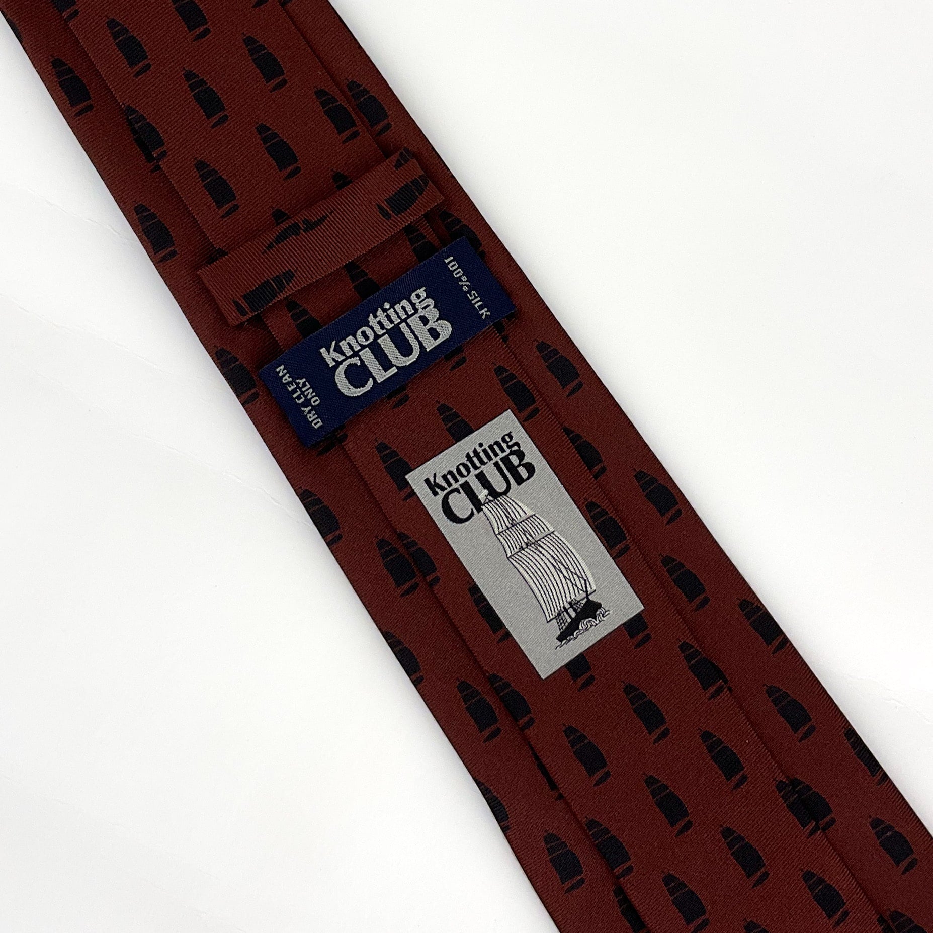 The back side of a burgundy red silk tie with a printed pattern of ships. The printed logo and and label of the tie is visible 