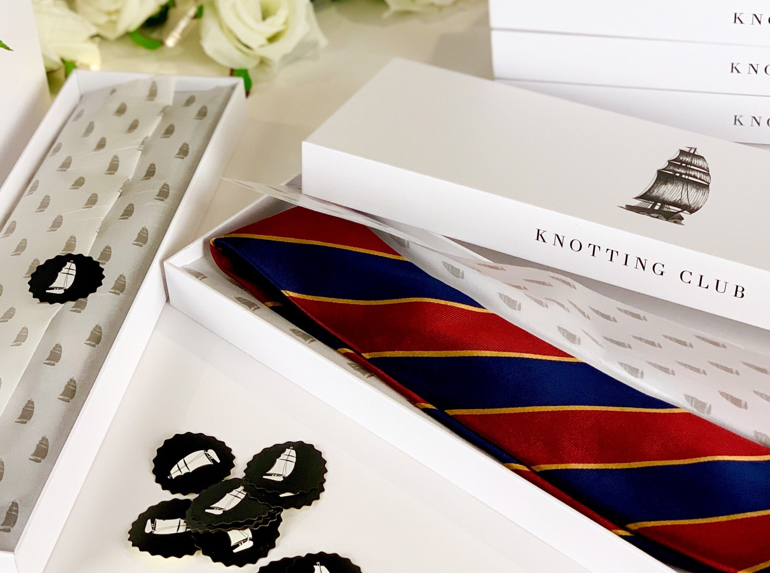 Mulberry Silk twill regimental tie with navy blue and red strikes and gold woven detailing lying in a tie box and wrapped with gift wrapping paper