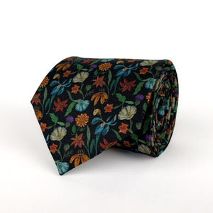 Mulberry silk twill tie with a multi-colored rainforest floral print on a black base rolled and placed on a white background