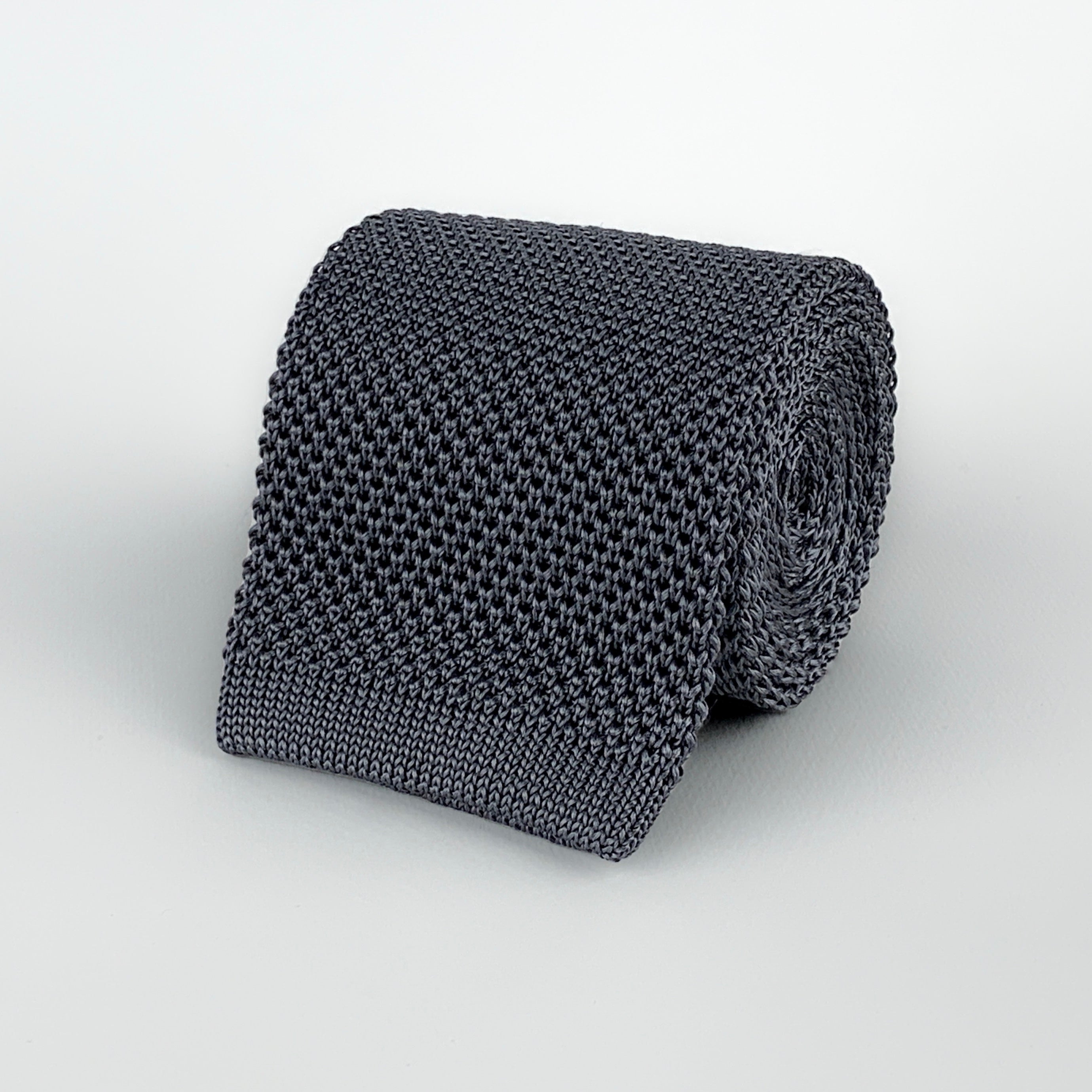 Dark grey mulberry silk knitted tie with a square end rolled and placed on a white background