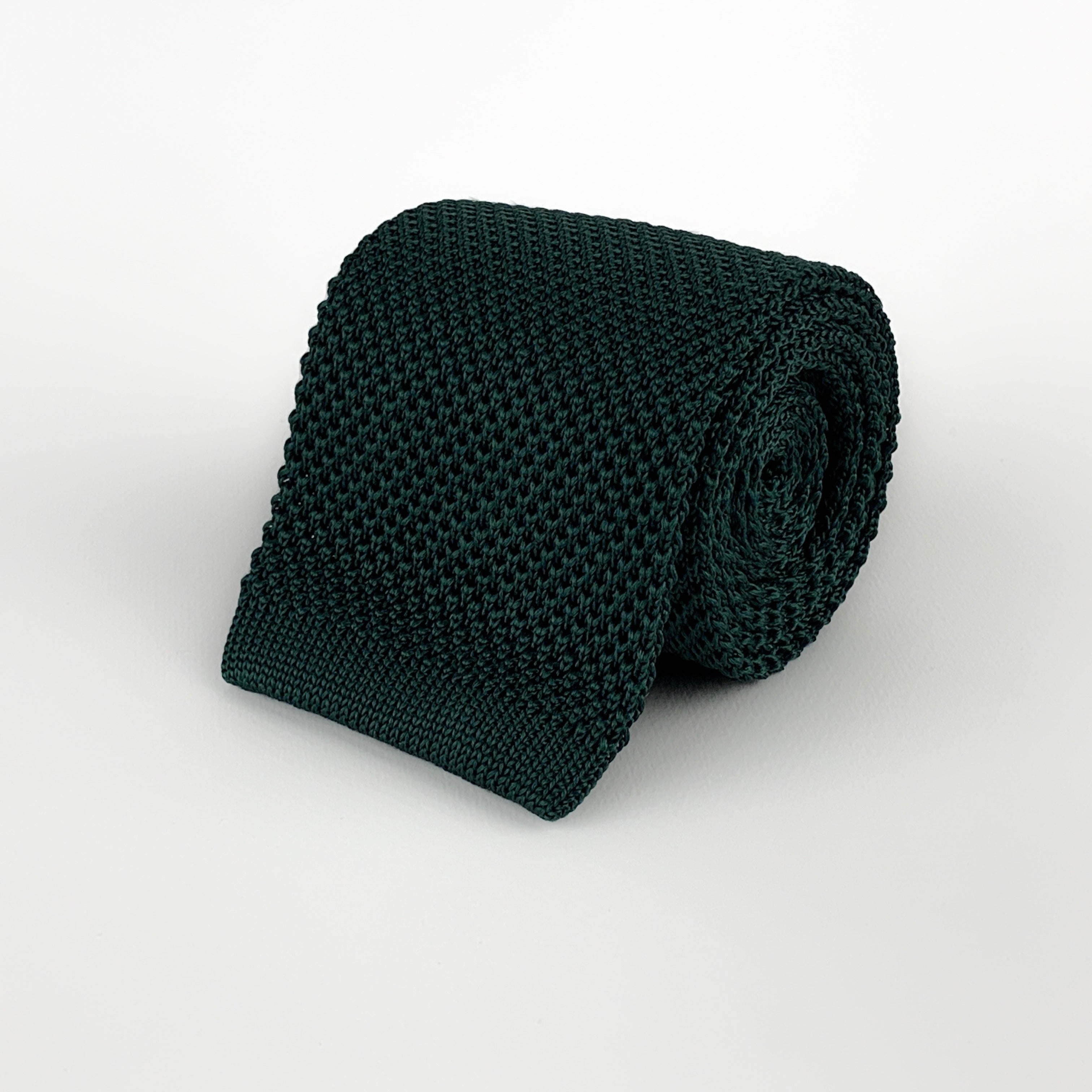 dark emerald green silk knitted tie with a square end, rolled and placed on a white background