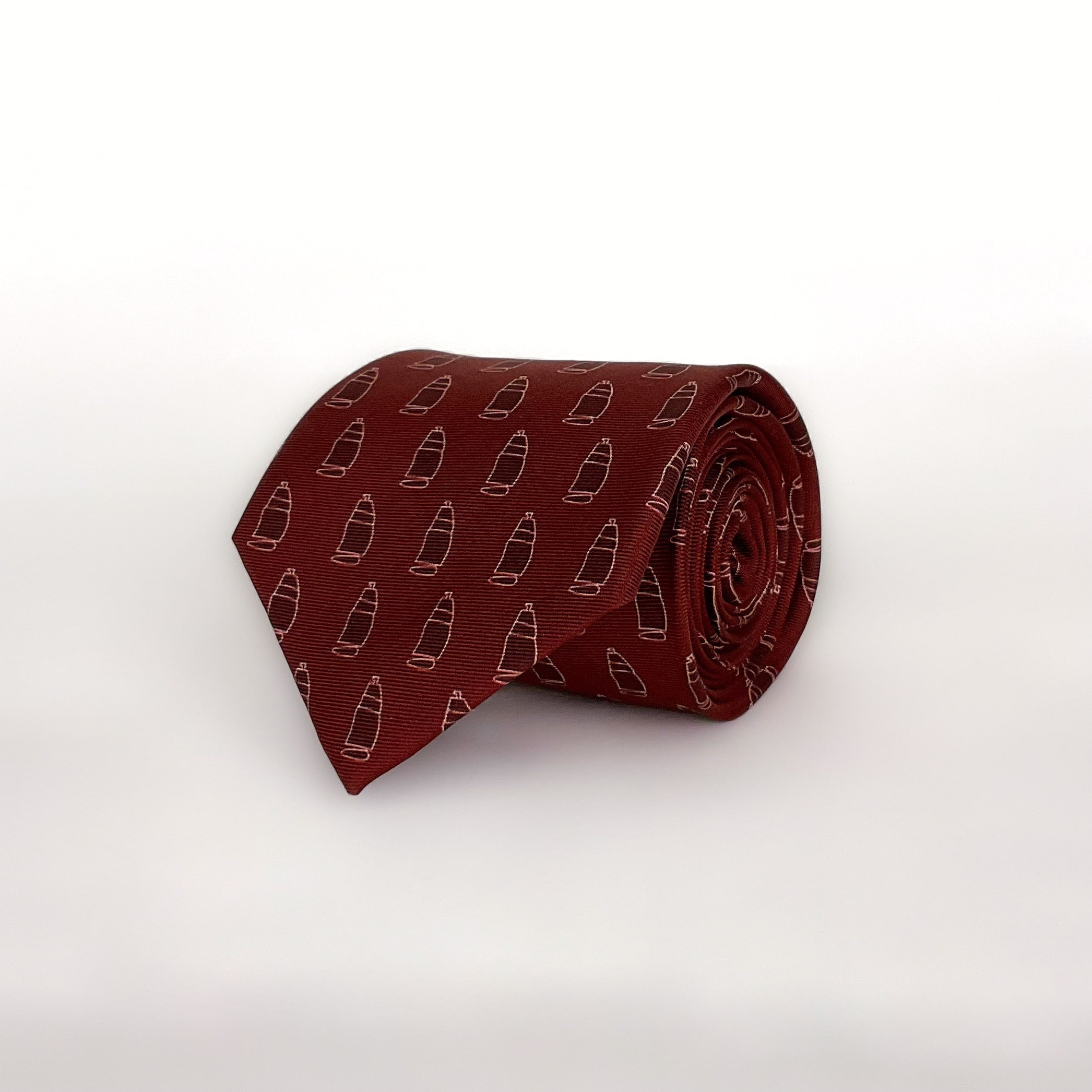 A burgundy red tie with a pattern of ships printed on it. The tie is rolled and placed on a white background.