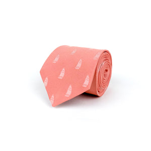 A flamingo pink mulberry silk twill tie with a woven pattern of ships in white ivory colour, rolled and placed on a white background