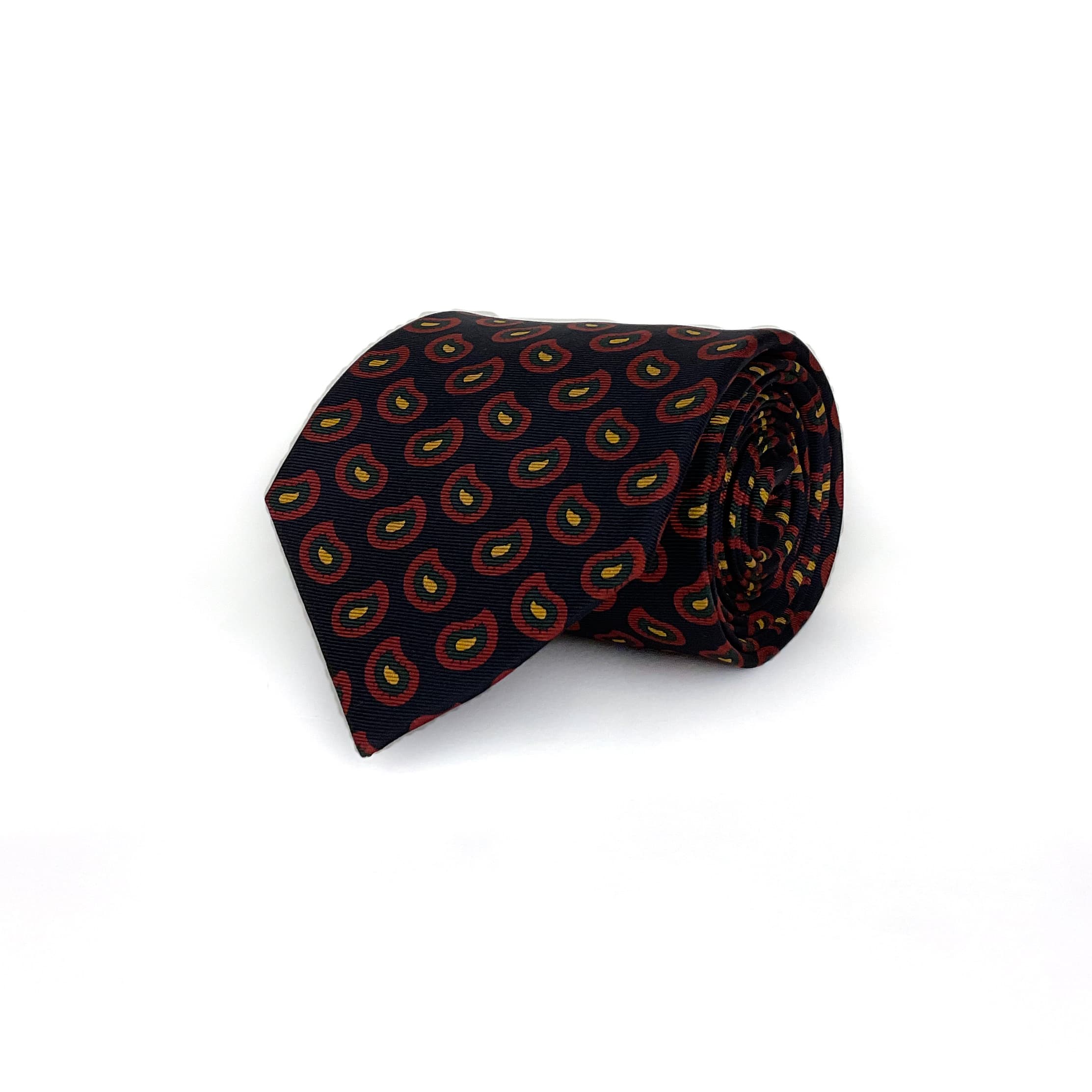 A paisley silk tie with a black base and red and yellow motifs  that is rolled and placed on a white background.