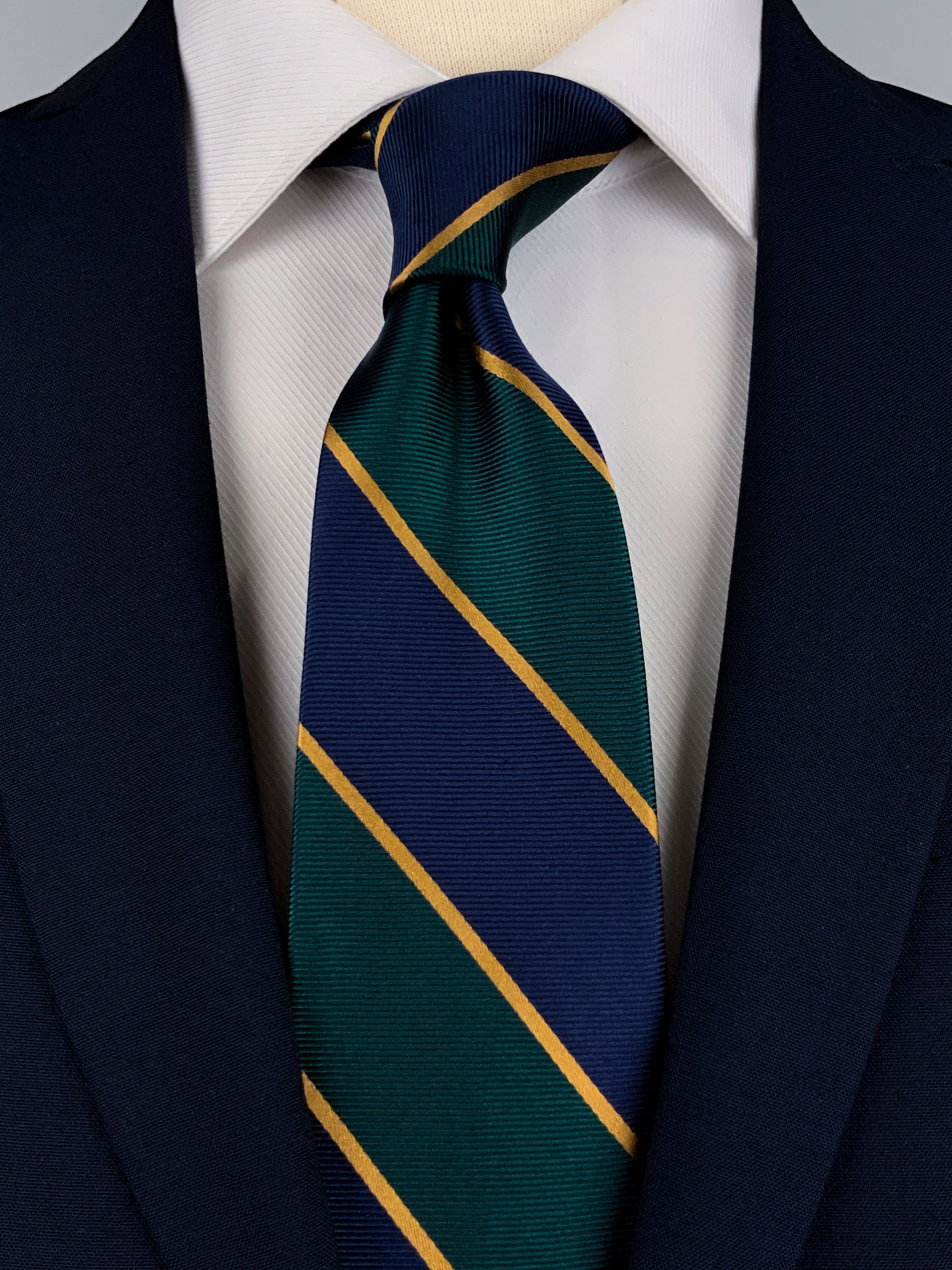 Mulberry silk twill tie with navy blue and dark emerald green regimental stripes and gold woven detailing worn with a white shirt and a navy blue suit