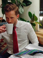 man at a cafe wearing a dark red mulberry silk satin tie on a white shirt and drinking coffee from a white mug