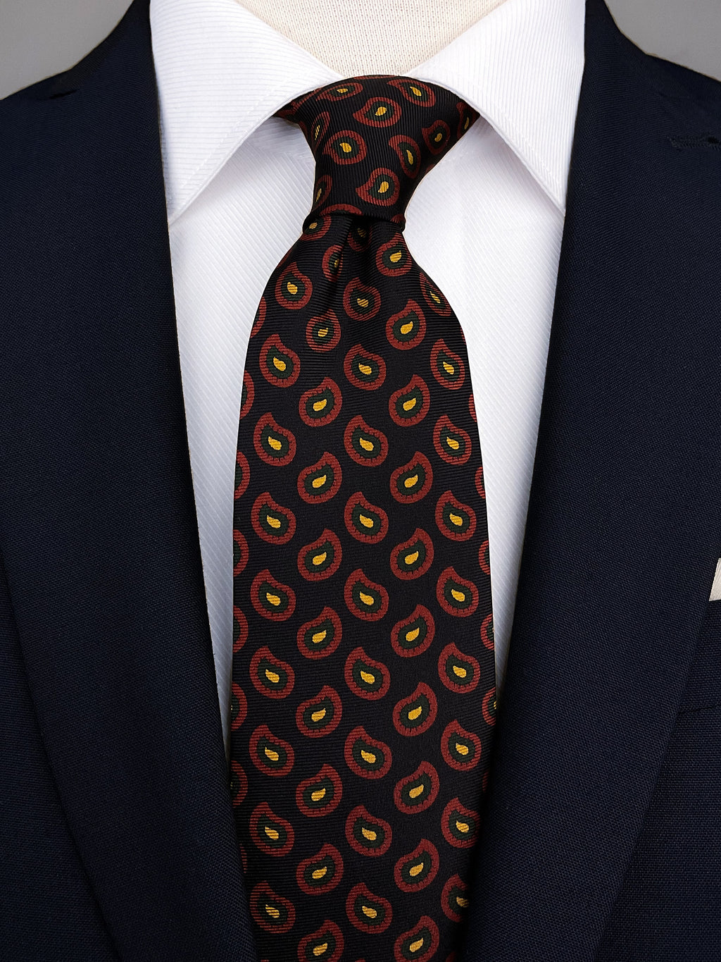 Paisley silk tie with a black base and red and yellow motifs. The tie is worn with a white shirt and a navy suit